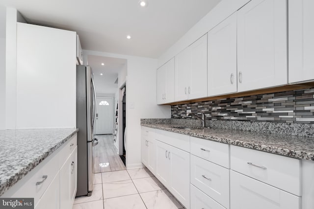 kitchen featuring stainless steel fridge, sink, white cabinets, and light stone countertops