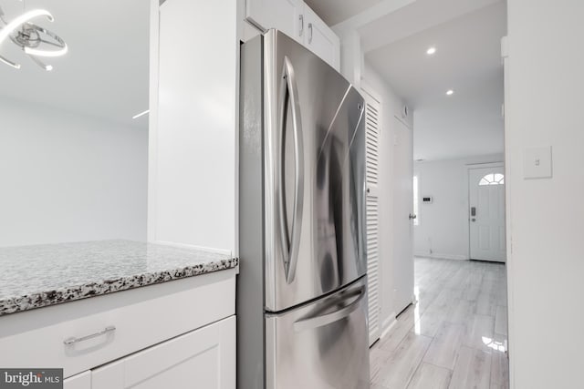 kitchen featuring white cabinets, stainless steel fridge, light stone countertops, and light hardwood / wood-style flooring