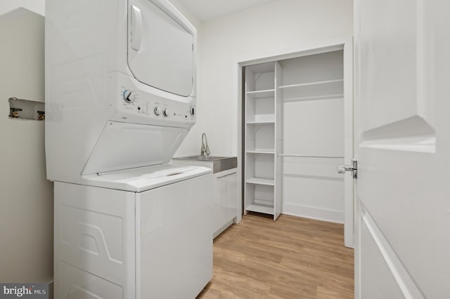 laundry room featuring cabinets, stacked washing maching and dryer, light hardwood / wood-style flooring, and sink