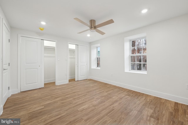 unfurnished bedroom featuring ceiling fan, multiple closets, and light hardwood / wood-style flooring