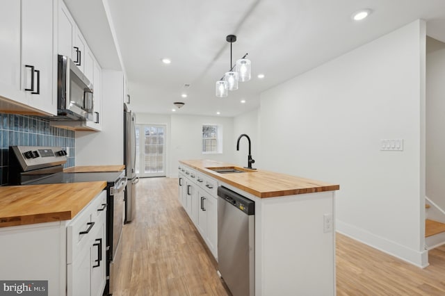 kitchen featuring butcher block countertops, white cabinetry, pendant lighting, and stainless steel appliances