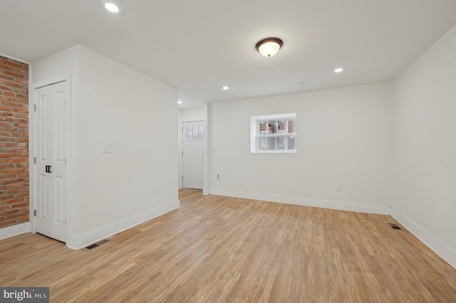 spare room featuring light wood-type flooring and brick wall