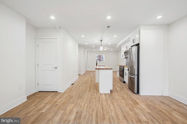 kitchen featuring white cabinetry, butcher block countertops, an island with sink, light wood-type flooring, and appliances with stainless steel finishes