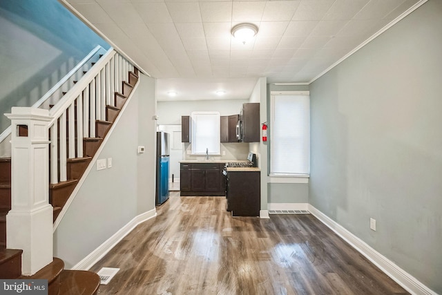 kitchen with dark brown cabinetry, crown molding, hardwood / wood-style flooring, black range with electric stovetop, and stainless steel refrigerator