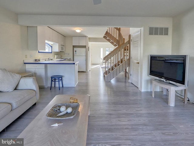 living area with stairway, visible vents, and wood finished floors