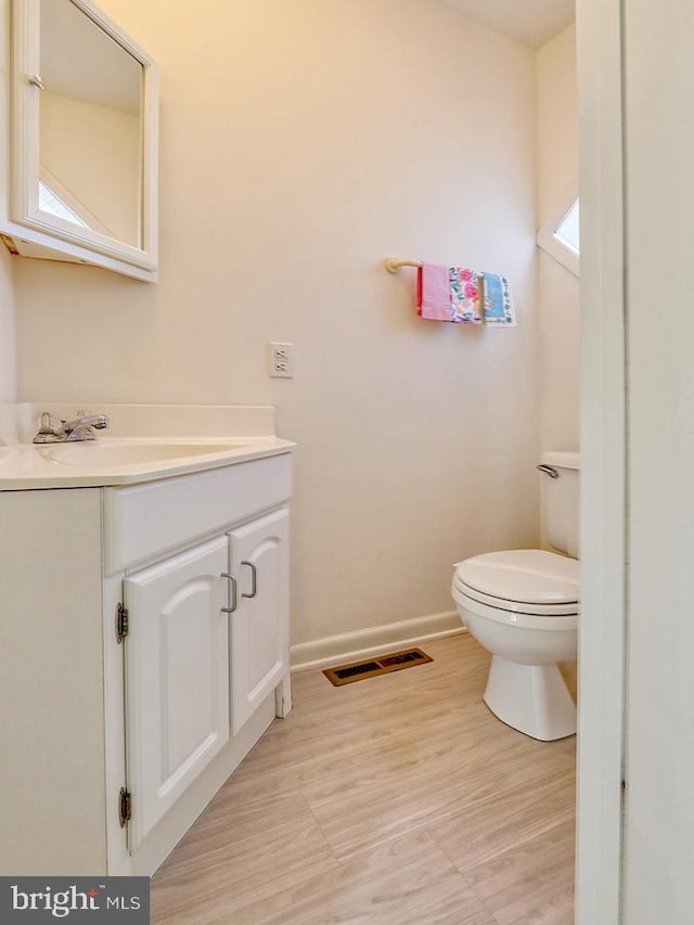 half bathroom with toilet, vanity, visible vents, and baseboards