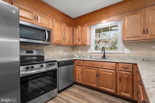 kitchen with light wood-type flooring, stainless steel appliances, light stone counters, and sink