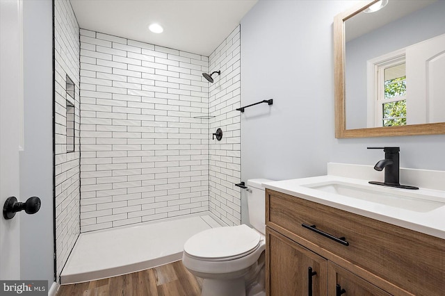 bathroom with a tile shower, vanity, hardwood / wood-style flooring, and toilet