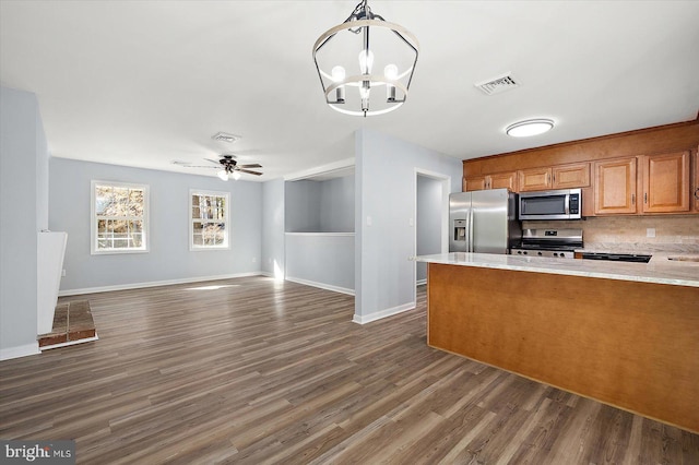 kitchen featuring dark hardwood / wood-style flooring, pendant lighting, decorative backsplash, ceiling fan with notable chandelier, and appliances with stainless steel finishes