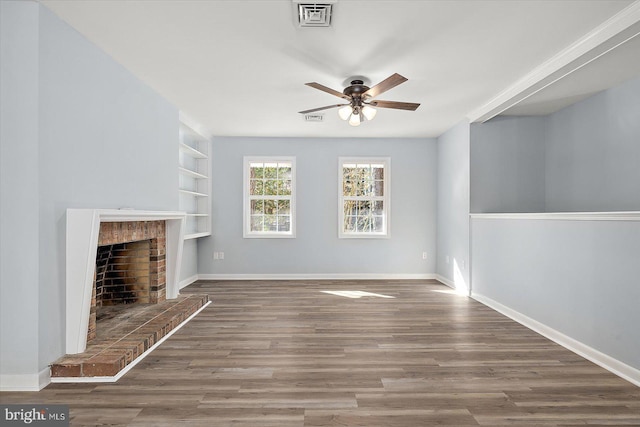 unfurnished living room featuring built in shelves, a brick fireplace, ceiling fan, and wood-type flooring