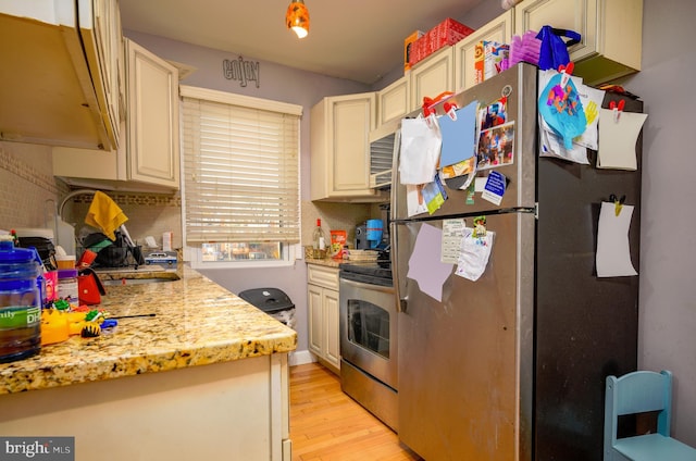 kitchen featuring backsplash, light stone counters, stainless steel appliances, cream cabinets, and light hardwood / wood-style floors