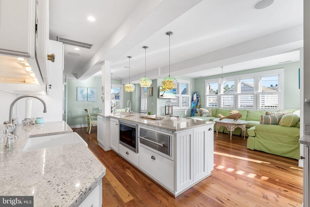 kitchen featuring light stone counters, a center island with sink, pendant lighting, and white cabinetry