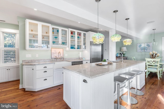 kitchen featuring dark wood-type flooring, a kitchen island with sink, high quality fridge, white cabinets, and sink