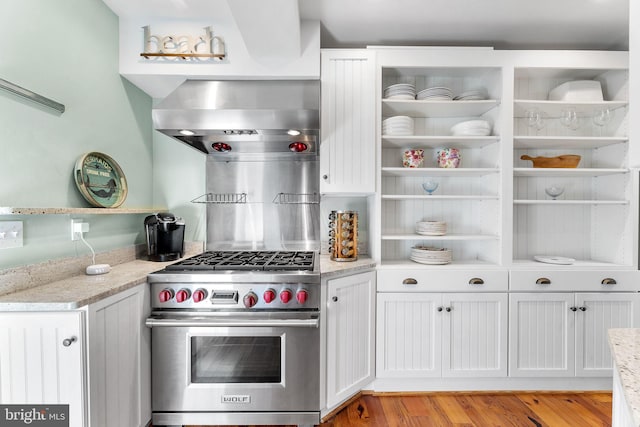 kitchen featuring light stone countertops, designer range, ventilation hood, and white cabinetry