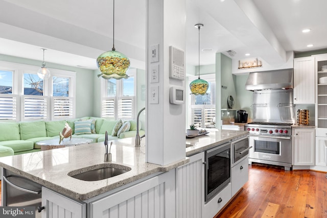 kitchen with stainless steel appliances, hanging light fixtures, light stone counters, wall chimney exhaust hood, and white cabinets