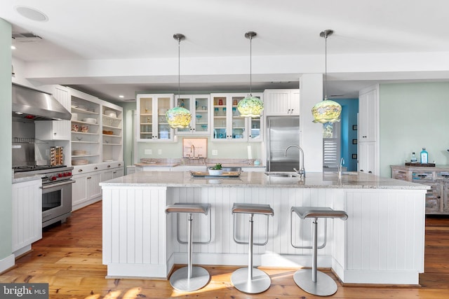 kitchen with sink, decorative light fixtures, white cabinets, extractor fan, and premium appliances