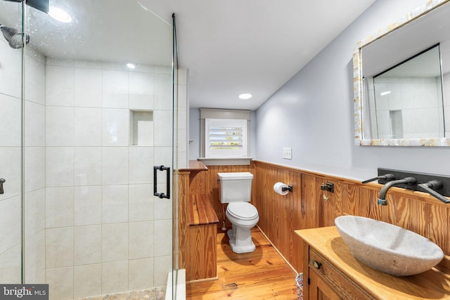 bathroom featuring wood walls, toilet, vanity, a shower with door, and hardwood / wood-style flooring