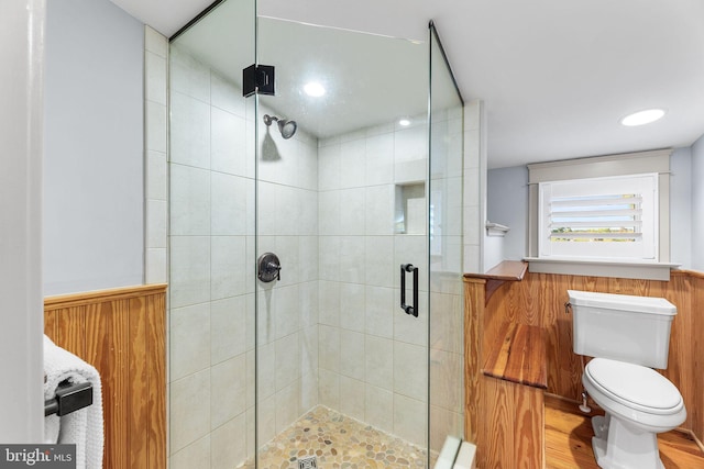 bathroom with wood-type flooring, wooden walls, an enclosed shower, and toilet