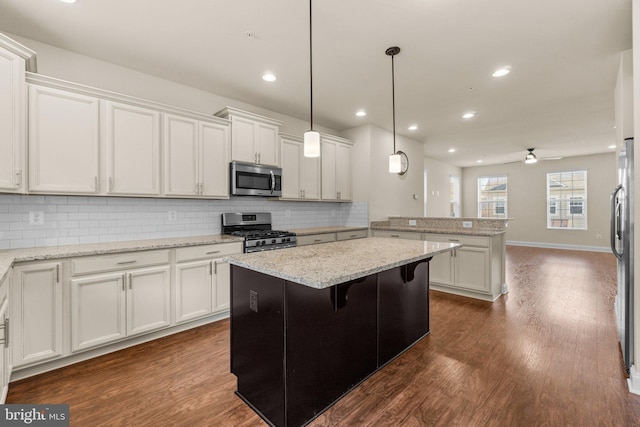 kitchen with a kitchen breakfast bar, stainless steel appliances, ceiling fan, decorative light fixtures, and a center island