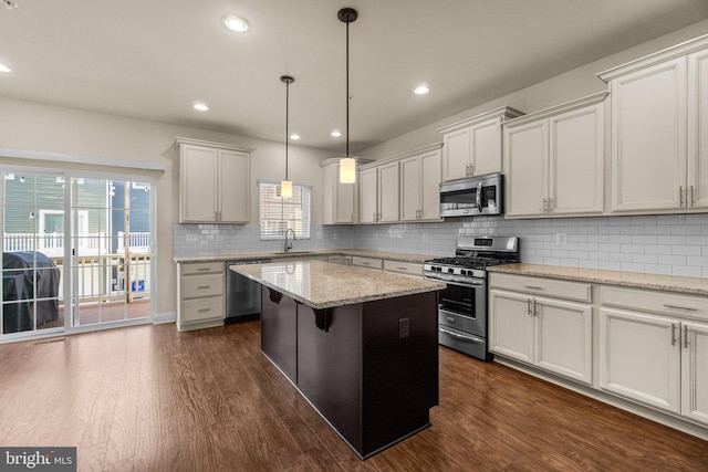 kitchen with pendant lighting, a center island, sink, light stone counters, and stainless steel appliances