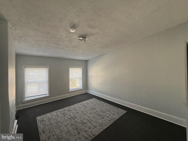 unfurnished room with dark carpet and a textured ceiling