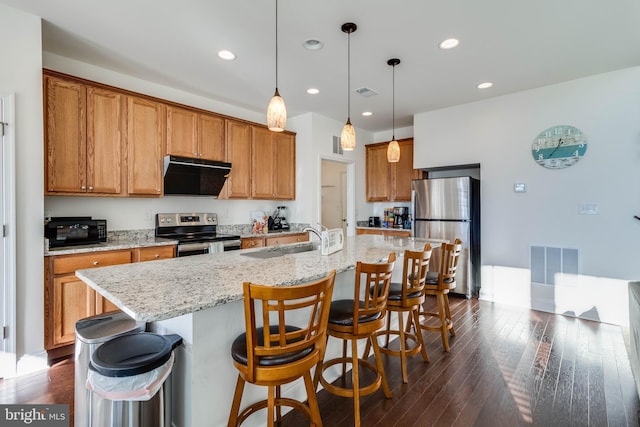 kitchen with dark hardwood / wood-style flooring, stainless steel appliances, a kitchen island with sink, sink, and hanging light fixtures