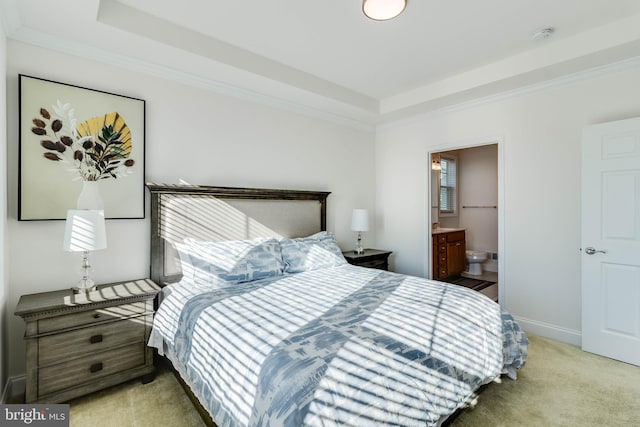 bedroom with a raised ceiling, connected bathroom, light colored carpet, and ornamental molding