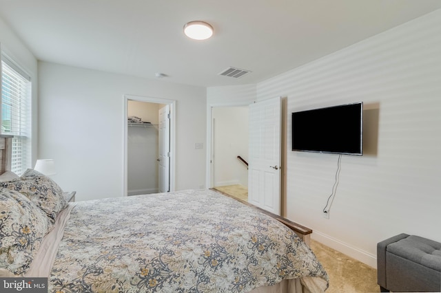 bedroom featuring a walk in closet, light carpet, and a closet