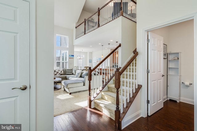 staircase featuring high vaulted ceiling, a chandelier, and hardwood / wood-style flooring