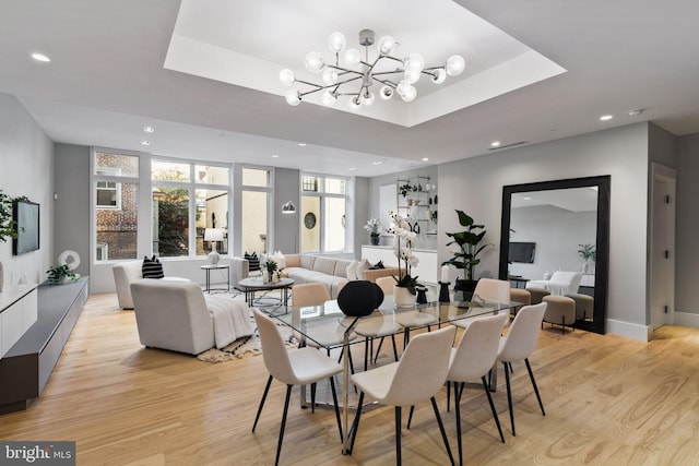 dining room featuring a raised ceiling, an inviting chandelier, and light hardwood / wood-style floors