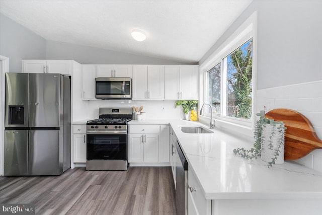 kitchen with white cabinetry, sink, stainless steel appliances, vaulted ceiling, and light wood-type flooring