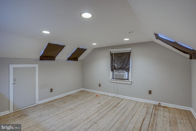 additional living space with cooling unit, vaulted ceiling, and light wood-type flooring