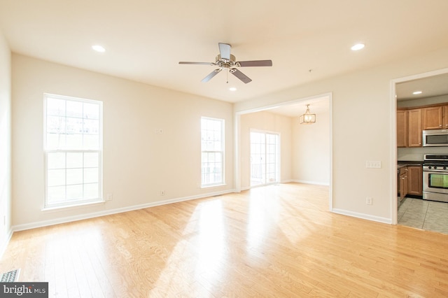 unfurnished living room with ceiling fan with notable chandelier, a healthy amount of sunlight, and light hardwood / wood-style floors