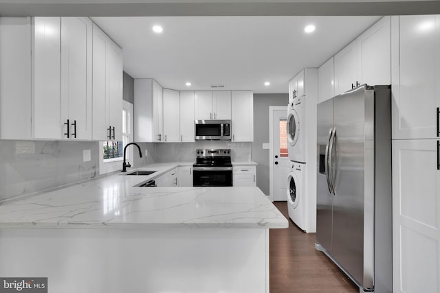 kitchen featuring light stone countertops, white cabinetry, stainless steel appliances, stacked washer / dryer, and kitchen peninsula