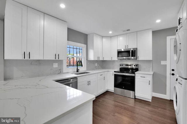 kitchen with stacked washing maching and dryer, stainless steel appliances, white cabinetry, and sink