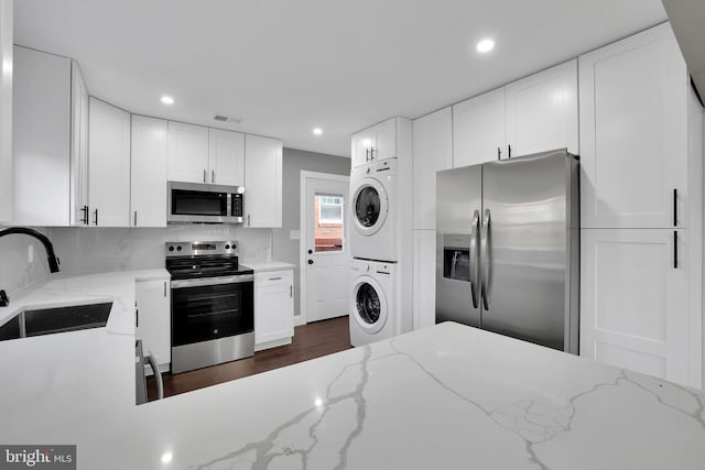 kitchen featuring stacked washer / drying machine, white cabinetry, sink, and appliances with stainless steel finishes