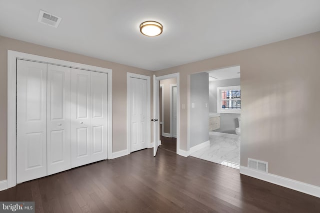 unfurnished bedroom featuring connected bathroom, dark hardwood / wood-style floors, and multiple closets