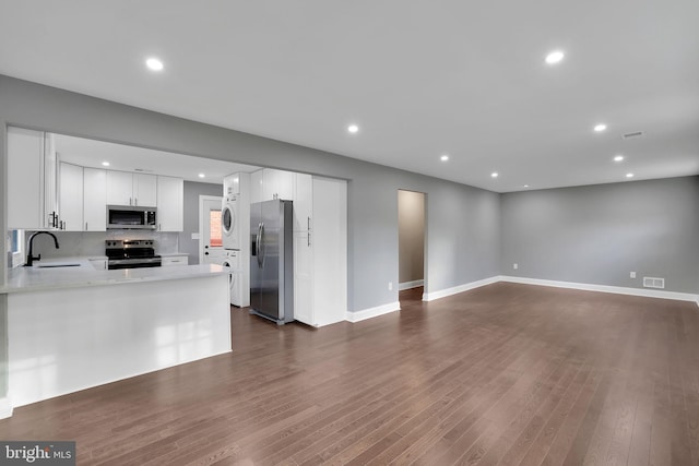 kitchen featuring dark hardwood / wood-style flooring, white cabinetry, stainless steel appliances, and stacked washer and clothes dryer