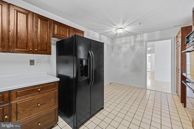 kitchen with black fridge with ice dispenser, light tile patterned flooring, and oven