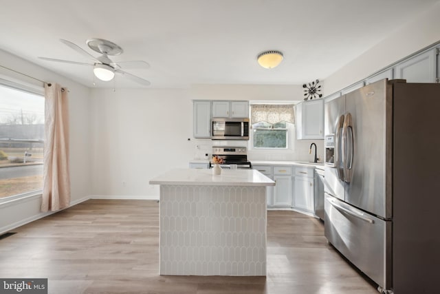 kitchen featuring sink, ceiling fan, a kitchen island, appliances with stainless steel finishes, and light hardwood / wood-style floors