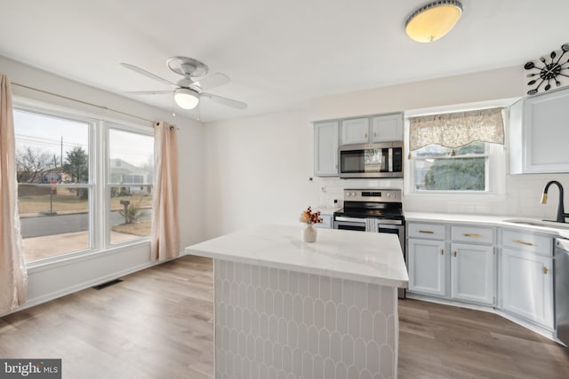 kitchen with tasteful backsplash, stainless steel appliances, sink, light hardwood / wood-style flooring, and a center island