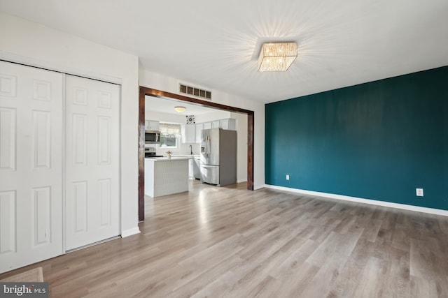 unfurnished living room featuring an inviting chandelier and light wood-type flooring