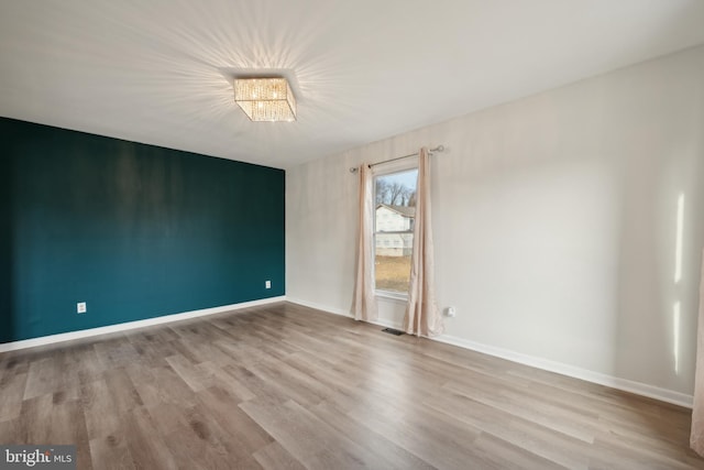 empty room with a notable chandelier and light hardwood / wood-style flooring