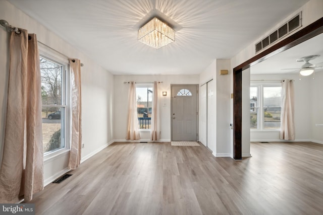 foyer with ceiling fan with notable chandelier, light wood-type flooring, and a wealth of natural light