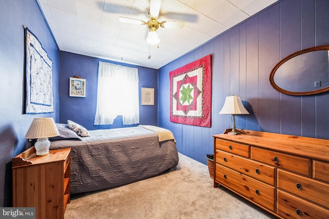 bedroom featuring ceiling fan, wood walls, and light colored carpet