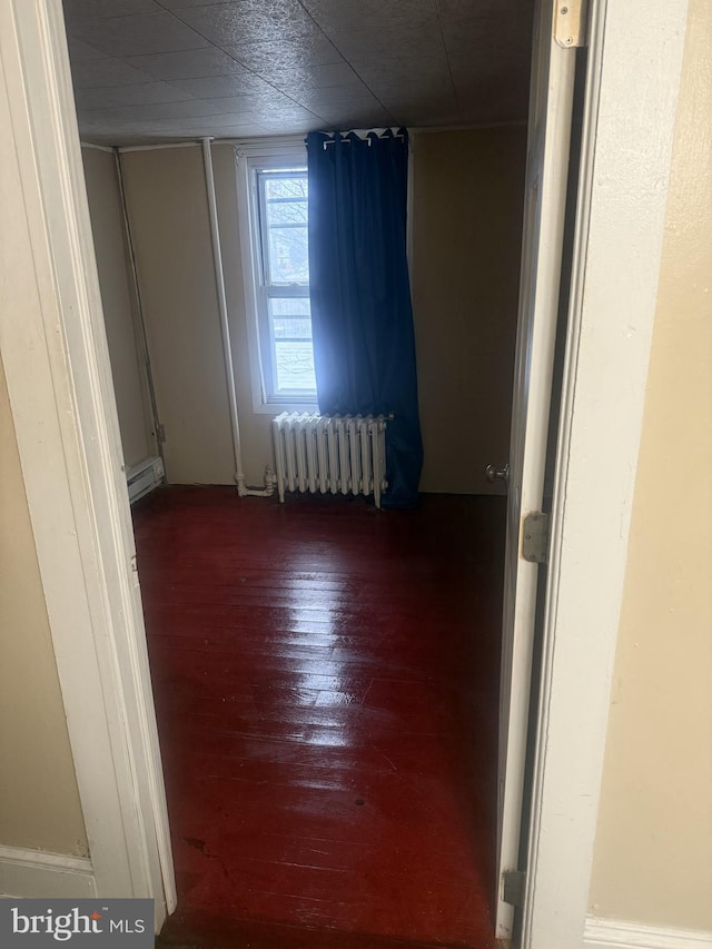 empty room with radiator, a baseboard radiator, and hardwood / wood-style flooring