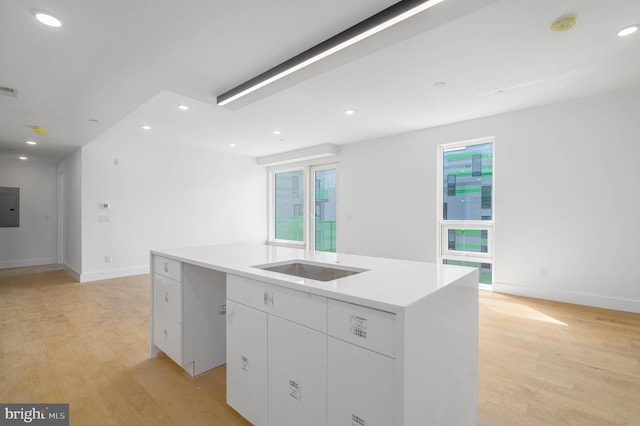 kitchen featuring white cabinetry, a kitchen island with sink, electric panel, and light hardwood / wood-style flooring