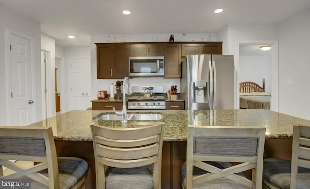 kitchen featuring light stone countertops, dark brown cabinets, stainless steel appliances, and a kitchen island with sink