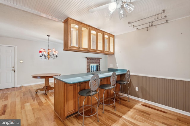 bar featuring pendant lighting, ceiling fan with notable chandelier, light hardwood / wood-style floors, and a brick fireplace