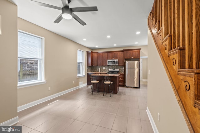 5738 Tulip St, Philadelphia, PA 19135 - kitchen featuring appliances with stainless steel finishes, a breakfast bar, decorative backsplash, a center island, and ceiling fan